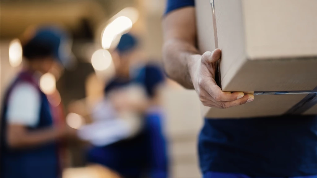 Close-up of a man carrying a moving box in a busy delivery environment